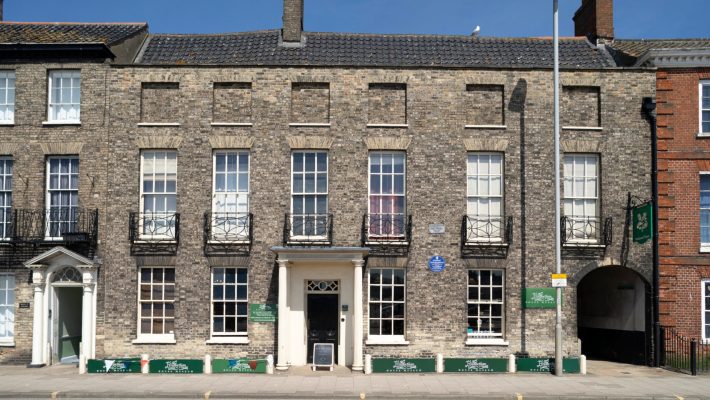 Historic brick building with white framed windows and signs on the ground floor in the UK under a clear blue sky