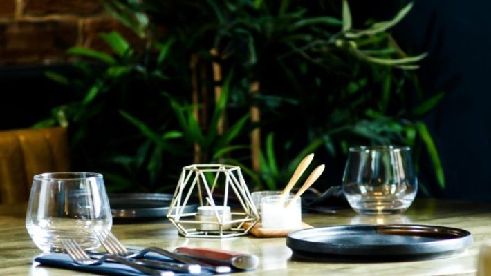 Elegant restaurant table setting with empty glasses, cutlery, candleholder, and plants in the background