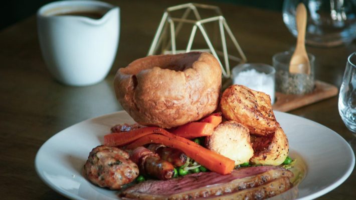 Traditional British roast dinner with Yorkshire pudding, roasted potatoes, carrots, and gravy on a white plate
