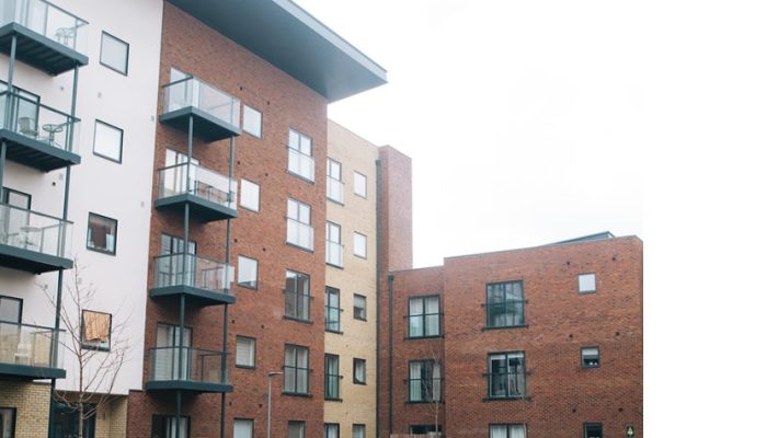 Modern apartment buildings with brick and glass balconies in an urban courtyard setting, featuring landscaped greenery