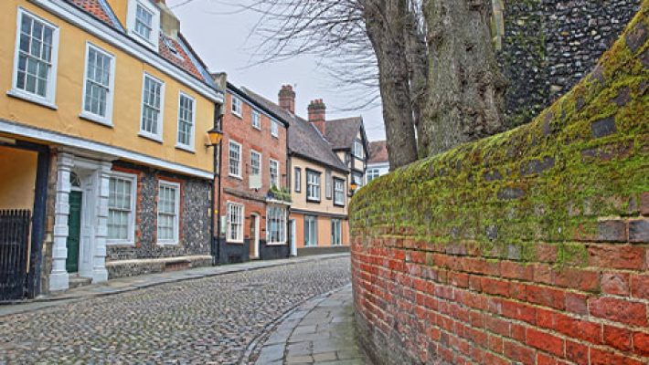 Quaint cobblestone street lined with historic buildings and moss-covered brick wall in a picturesque UK town