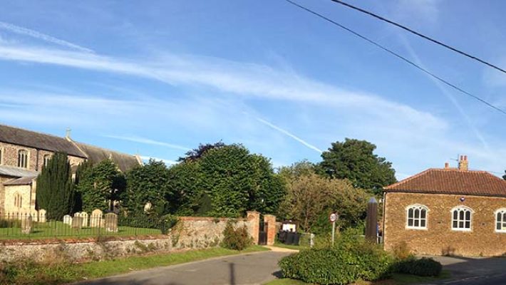 Historic English church and village scene with clear blue sky and lush greenery