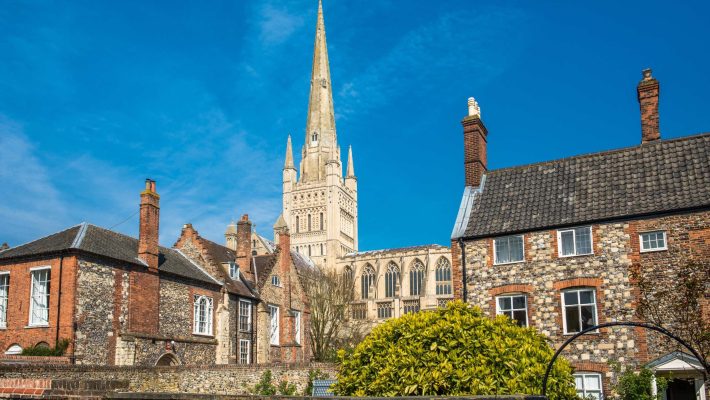 Historic cathedral spire towering above traditional English buildings under a clear blue sky