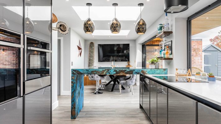 Modern kitchen with sleek cabinets, blue island and pendant lights, large windows opening to a garden view