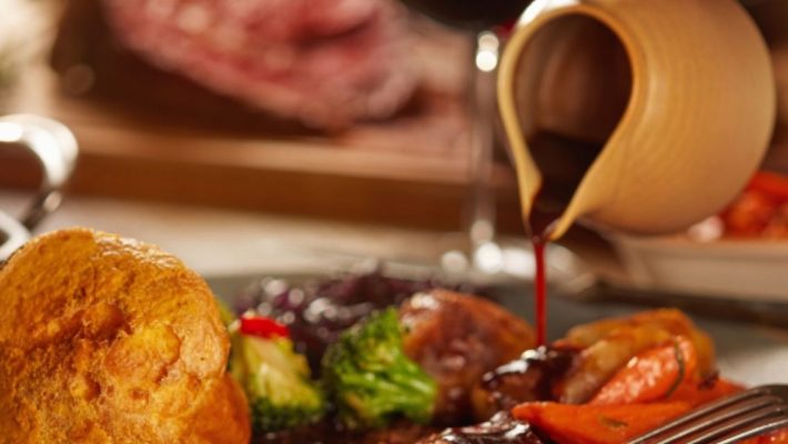 Traditional Sunday roast with Yorkshire pudding and gravy being poured, served with vegetables and potatoes