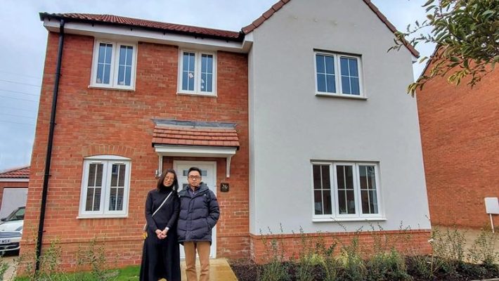 Couple standing outside their newly purchased two-storey red brick and white house in the UK