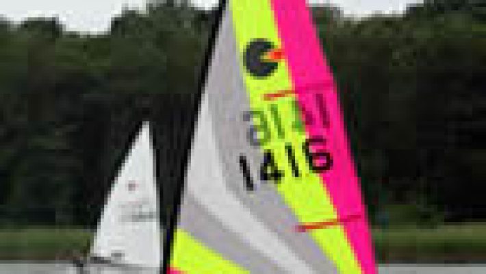 Sailboats with colourful sails racing on a lake with a forested background under cloudy skies