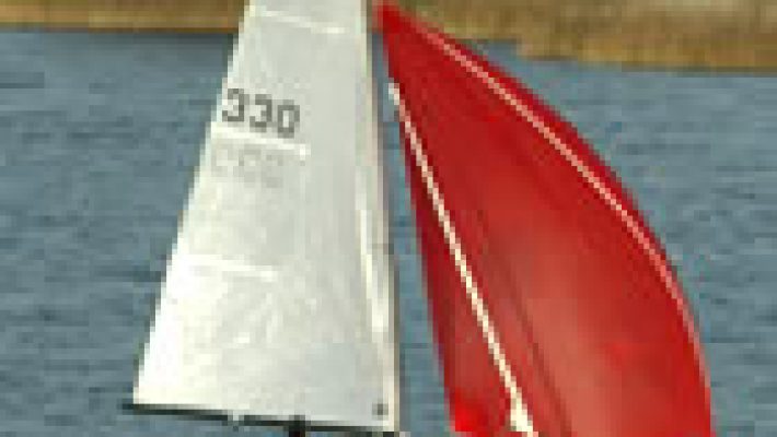 Red and white sailboat gliding on a lake with lush green trees in the background on a clear day