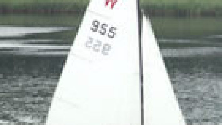 Sailing boat with white sails on a calm lake surrounded by trees in the background