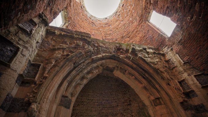 Looking up at the ancient brick interior of a historic archway with a circular opening and intricate stone carvings