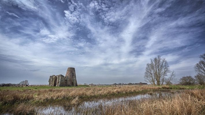Ancient English ruin by marshland under dramatic cloudy sky in countryside landscape