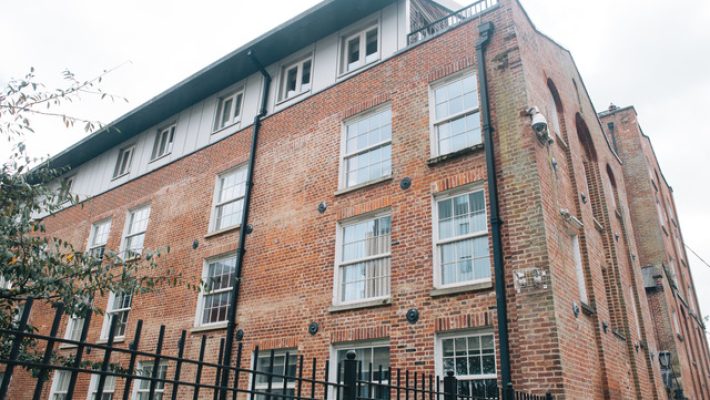 Red brick building with multiple windows and a black iron fence in front, offering a classic architectural design