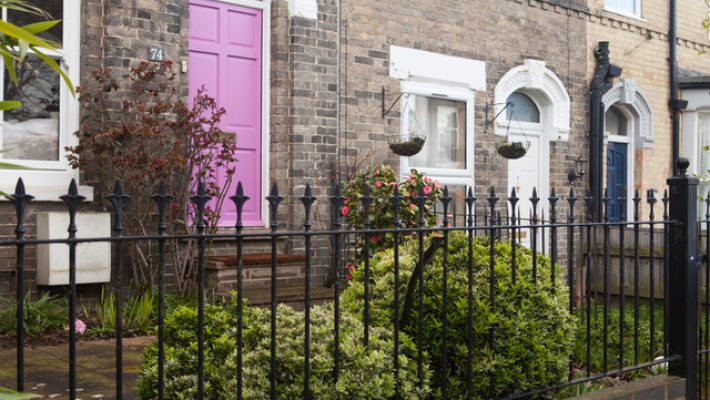 Terraced house with purple door and garden, surrounded by black metal fence in quaint UK neighbourhood