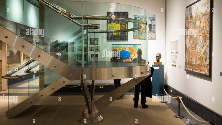 Modern museum interior with spiral staircase, artwork, and sculptures in a well-lit exhibition space