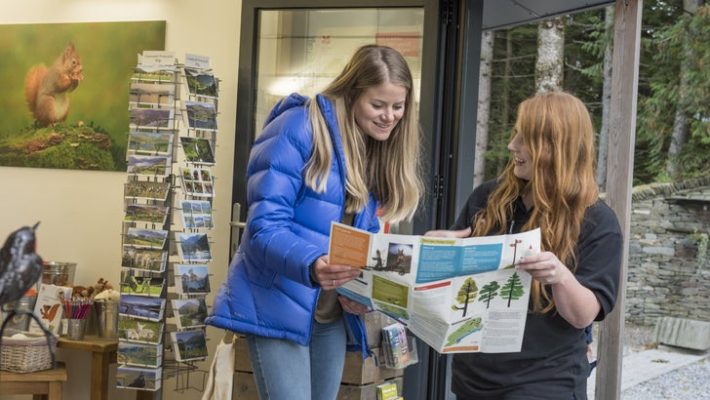 Two women in a visitor centre reading a brochure, surrounded by postcards and nature art